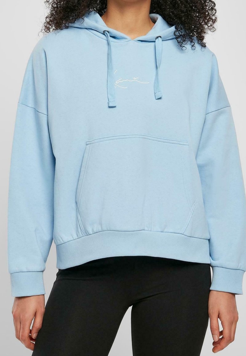 Ljust blå huvtröja av mjukt material, med en känguruficka, ribbade muddarna och en diskret broderad design på bröstet.