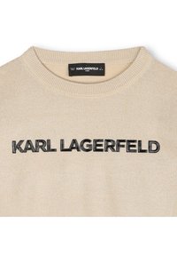 Bež pleten pulover z okroglim izrezom, na sprednji strani z izrazitim črnim logotipom "KARL LAGERFELD". Gladek tekstura.