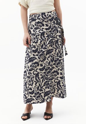 Beige Wickelrock mit großem schwarzem Blumenmuster, befestigt mit einer schwarzen Schnalle, getragen mit schwarzen offenen Absatzschuhen.