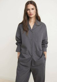 Camisa gris de botones con cuello, mangas largas y dos bolsillos frontales. Fabricada con un tejido suave, presenta un corte relajado y costuras minimalistas.