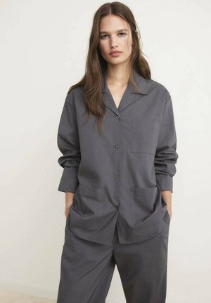 Chemise grise à boutons, avec un col, des manches longues et deux poches frontales. Fabriquée en tissu lisse, avec une coupe décontractée et des coutures minimalistes.