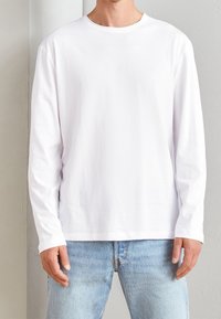 Camiseta blanca de manga larga en suave tela de algodón, con cuello redondo y diseño simple, combinada con unos vaqueros de denim azul claro.