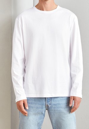 Vit långärmad t-shirt i mjukt bomullstyg, med rund hals och enkel design, kombinerad med ljusblå denimjeans.