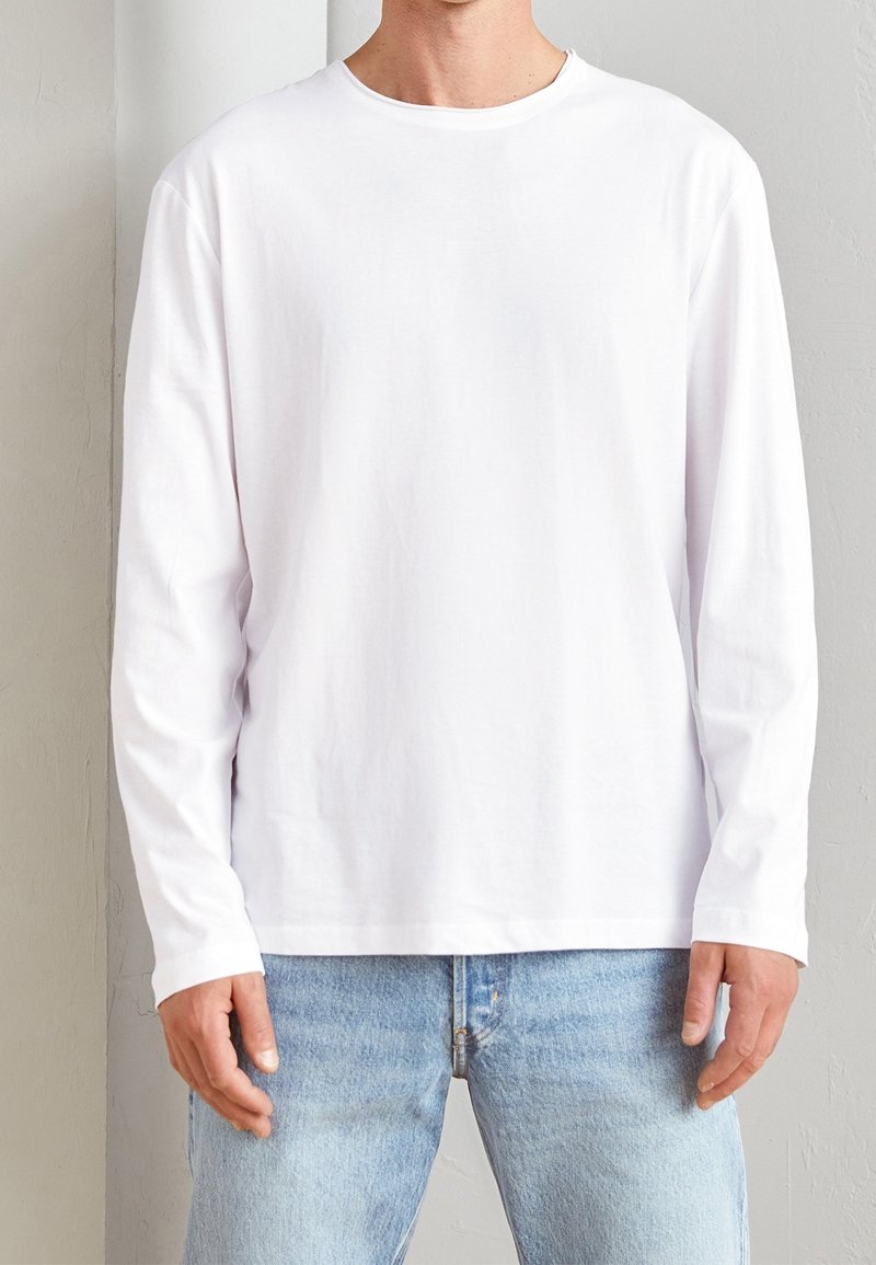Camiseta blanca de manga larga en suave tela de algodón, con cuello redondo y diseño simple, combinada con unos vaqueros de denim azul claro.