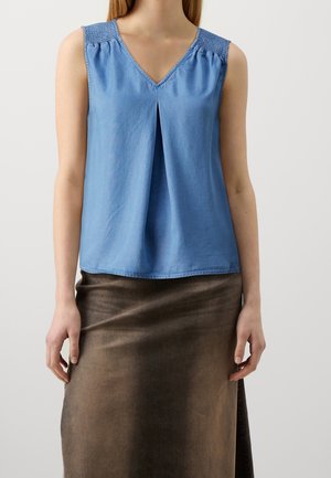 Haut sans manches bleu avec un décolleté en V et des détails de plis. Présente des épaules smockées et un tissu doux et léger. Porté avec une jupe marron.