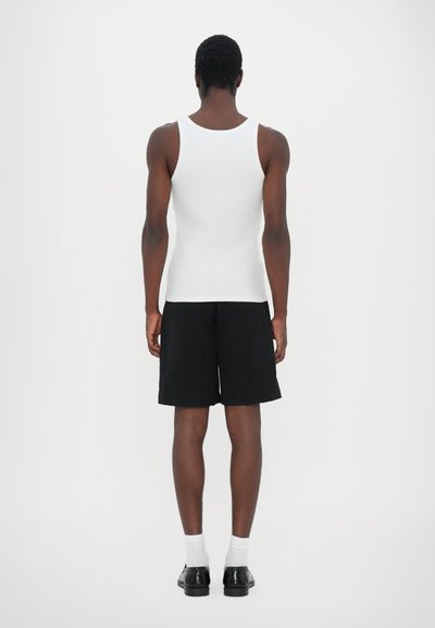 Un débardeur blanc sans manches associé à un short noir, complété par des chaussures noires et des chaussettes blanches. Design minimaliste, texture lisse.