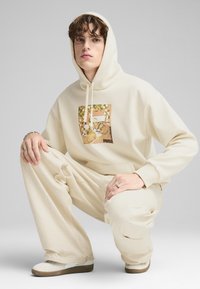 Bežinė džemperis su grafinio dizaino tigro vaizdu, derinamas su atitinkančiomis plačiomis kelnėmis ir šviesiomis sportbačiais.