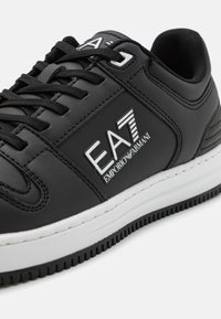 Sneaker in pelle sintetica nera con suola bianca, dettagli del logo e cuciture decorative sui lati. Design con lacci e occhielli rinforzati.