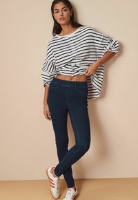 Top de rayas blancas y marinas, de corte oversize, que deja al descubierto el abdomen, combinado con jeans skinny azul oscuro y zapatillas blancas con rayas rojas.