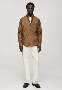 Brown button-up shirt with a chest pocket, paired with white trousers and black shoes. Simple design, smooth texture, and tailored fit.