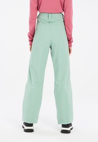 Mintgroene, high-waisted broek met een relaxte pasvorm en subtiele textuur, gecombineerd met zwart-witte sneakers. Minimalistisch ontwerp, geen zichtbare patronen.