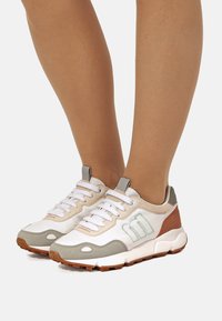 Sneakers atletiche con tomaia in mesh bianca, dettagli in suede grigio chiaro, tallone marrone e suola in gomma rigata. Caratterizzate da lacci e dettaglio del logo.