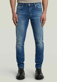 Blå denimjeans med slim fit, bleknade detaljer, fem fickor och metallbeslag. Matchas med svarta ankellånga stövlar.