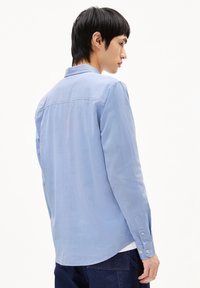 Light blue long-sleeve shirt made of smooth fabric, featuring a button-down collar and cuffs, with a curved hem and a single back seam.