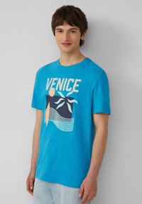Blaue Baumwoll-T-Shirt mit grafischem Druck mit dem Text "VENEDIG", abstrakten Formen und Palmenblättern, kurzen Ärmeln und rundem Ausschnitt.