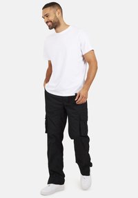 Biała bawełniana koszulka zestawiona z czarnymi spodniami cargo. Spodnie mają wiele kieszeni i luźny krój, dopełnione białymi sneakerami.