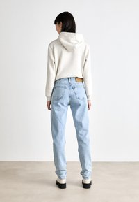 Lichtgrijze hoodie met capuchon, gecombineerd met hooglopende, lichtblauwe denim jeans. Stevige zwarte plateau-laarzen. Minimalistische, casual look.