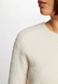 Morbido maglione color crema con una texture pelosa. Presenta un collo rotondo e maniche raglan, con una ripresa ravvicinata dell'area della spalla.