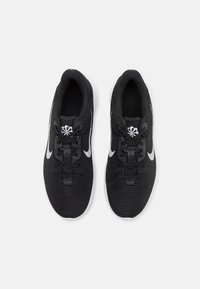 Scarpe sportive nere con una tomaia in mesh testurizzato, dettagli bianchi e lacci neri. Presentano una suola imbottita e un design a punta rotonda.