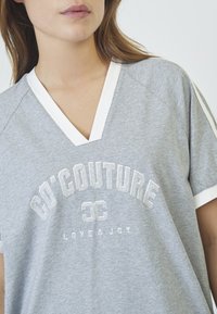 Pilkas trumpas rankovėmis T-shirt su V formos iškirpte, baltu apvadu ir atspausdintu logotipu "GO'COUTURE LOVE & JOY" metalizuotais rašmenimis priekyje.