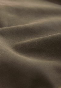 Brown fabric with a soft, textured surface, displaying gentle folds and a smooth appearance, highlighting its pliability and material quality.