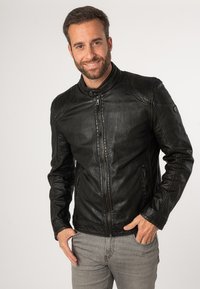 Schwarze Leder-Motorradjacke mit hohem Kragen, strukturierten Schulterakzenten und Reißverschluss-Taschen. Getragen über grauen Jeans.
