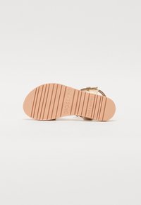 Sandale à lanières avec une semelle en caoutchouc rose texturé, dotée d'une partie supérieure en métal doré et d'une sangle réglable. Lignes de semelle transparentes pour une meilleure adhérence.