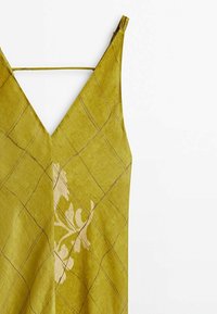 Robe sans manches en lin vert avec fines bretelles, décolleté en V, motif en grille diagonale et léger motif floral sur le côté avant gauche.