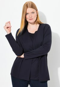 Donkerblauwe lange mouwen top met een ronde halslijn en een gelaagd ontwerp, gemaakt van soepel stof en een comfortabele pasvorm, gecombineerd met donkere spijkerbroeken.