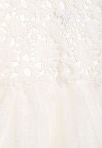 Weißes Kleid mit einem floralen Spitzenoberteil und einem weichen Tüllrock mit dezentem Schimmer. Verziert mit Stoffblumen und feinen Nähten.