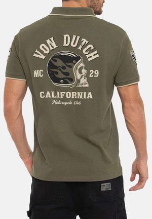 Homme portant un polo vert olive avec le texte "Von Dutch California Motorcycle Club" et un graphique de crâne avec casque en flammes au dos.