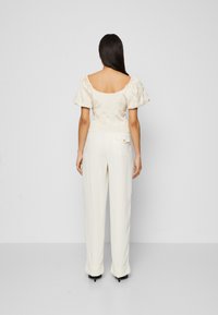 Top bianco testurizzato con maniche a sbuffo e una scollatura larga sul retro, abbinato a pantaloni larghi crema con tasca e dettagli in bottone.