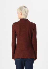 Top cu mânecă lungă, guler înalt, realizat dintr-un material roșu închis cu un finisaj texturat. Prezintă un tiv curbat și un design slim fit.