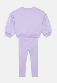 Lila dvodelna kombinacija, ki obsega kratko pulover s puhastimi rokavi in usklajene legice iz mehkega, teksturiranega materiala.