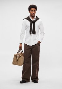 Beežikas duffel-kott pruunide detailidega, valge nööbitav särk, pruun kampsun üle õla visatud ja laiad pruunid püksid. Kingad on mustad ja sileda tekstuuriga.