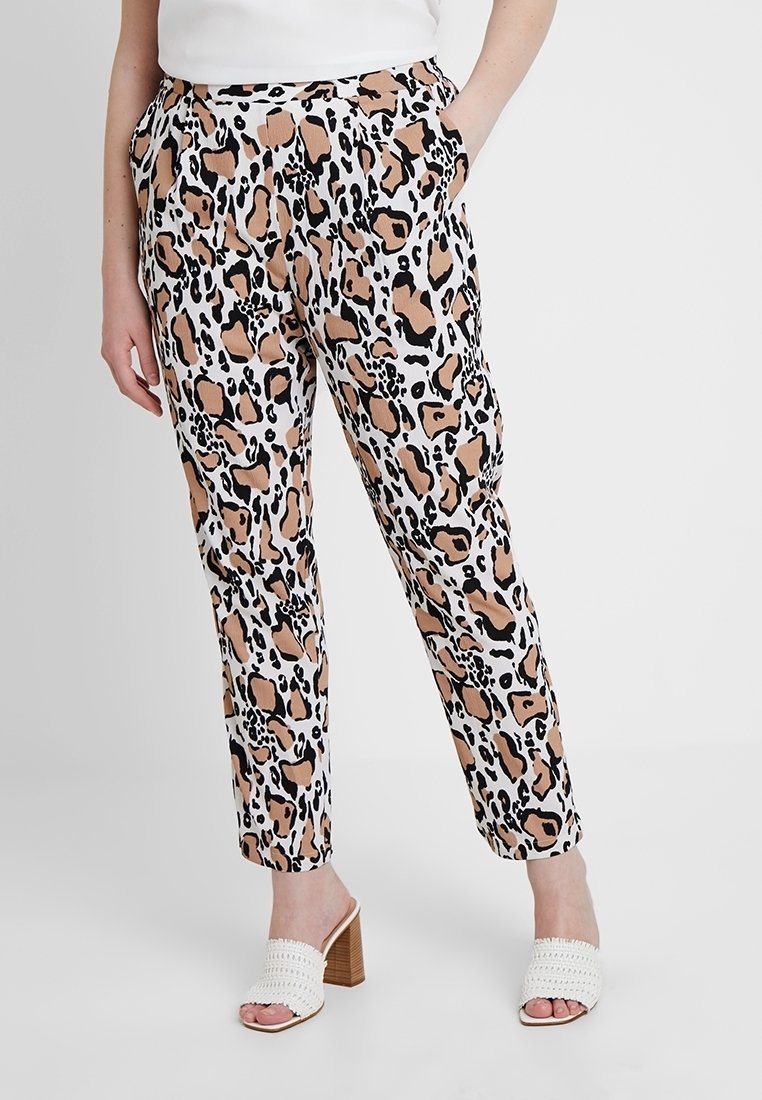 Pantalon imprimé léopard en beige clair, noir et blanc, avec poches latérales et coupe décontractée, associé à des sandales blanches tissées à talon bloc.
