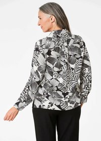 Blusa a maniche lunghe con stampa floreale bianca e nera, caratterizzata da un tessuto liscio, colletto strutturato e dettagli con bottoni lungo la schiena.