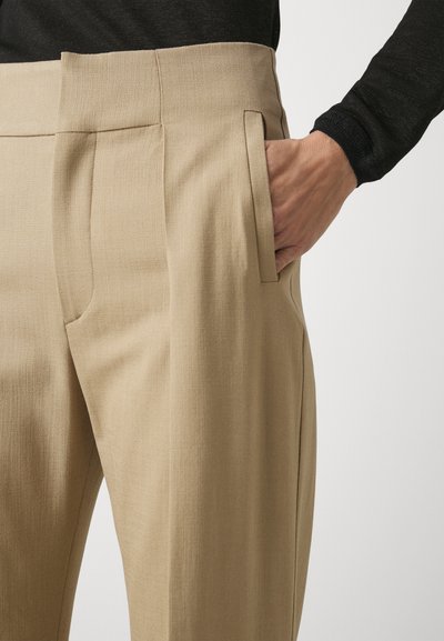 Beige broek met een gladde textuur, voorzien van een platte tailleband, zijzakken en een getailleerde pasvorm. Gepaard met een zwart langmouwen top.