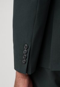 Dark green suit jacket sleeve with four black buttons and subtle stitching details on the cuff. Material appears smooth and tailored.