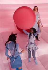 Trois personnes jouent avec une grande balle rouge sur une surface gonflable rose, vêtues de différentes nuances de bleu et de gris, avec des textures et des détails.