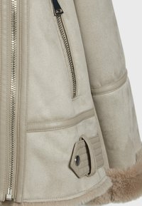 Beige faux suede jacket with a zippered front, side pockets, and a fur-lined hem. Features stitched accents and a durable metal zipper.