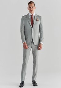 Jasnoszary garnitur o dopasowanym kroju, biała koszula, czerwona krawat w wzory oraz chusteczka w kieszonce. Czarny obuwie dopełnia całość.