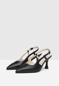 Decolletè slingback in pelle nera con punta affusolata, cinghie sottili, fibbie regolabili e tacco alto affusolato. Texture liscia e design minimalista.