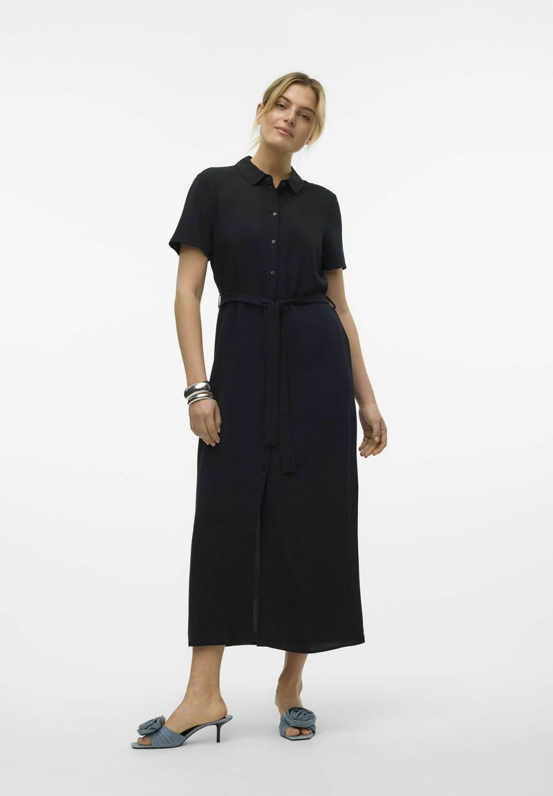 Robe chemise marine à manches courtes avec des boutons, dotée d'une ceinture à la taille. Porter avec des sandales à talons bleu clair, ornées d'accents roses.