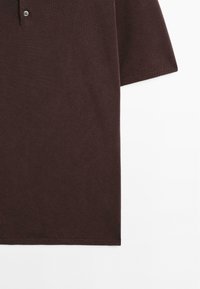 Polo marrone con tessuto a maglia testurizzata, caratterizzato da un colletto con due bottoni e maniche corte. Rifinito con polsini a costine.