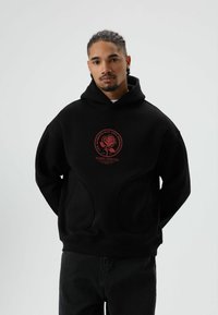 Zwarte hoodie met een grote rode roos afbeelding en tekst op de voorkant. Voorzien van een buidelzak en geribbelde boorden en zoom.