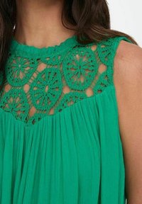 Abito verde con gonna plissettata e yoke in pizzo all'uncinetto con motivi floreali. Tessuto morbido e leggero.