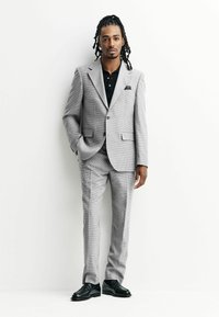 Gray houndstooth suit with a single-breasted jacket, matching trousers, and a black polo shirt. Black leather shoes and pocket square.