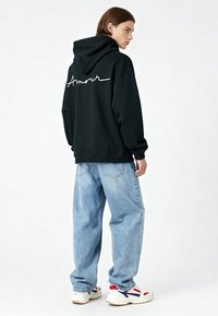 Sudadera negra con el texto "Amour" en blanco en la parte posterior, combinada con unos vaqueros ligeros de corte holgado y zapatillas blancas con acentos rojos y azules.