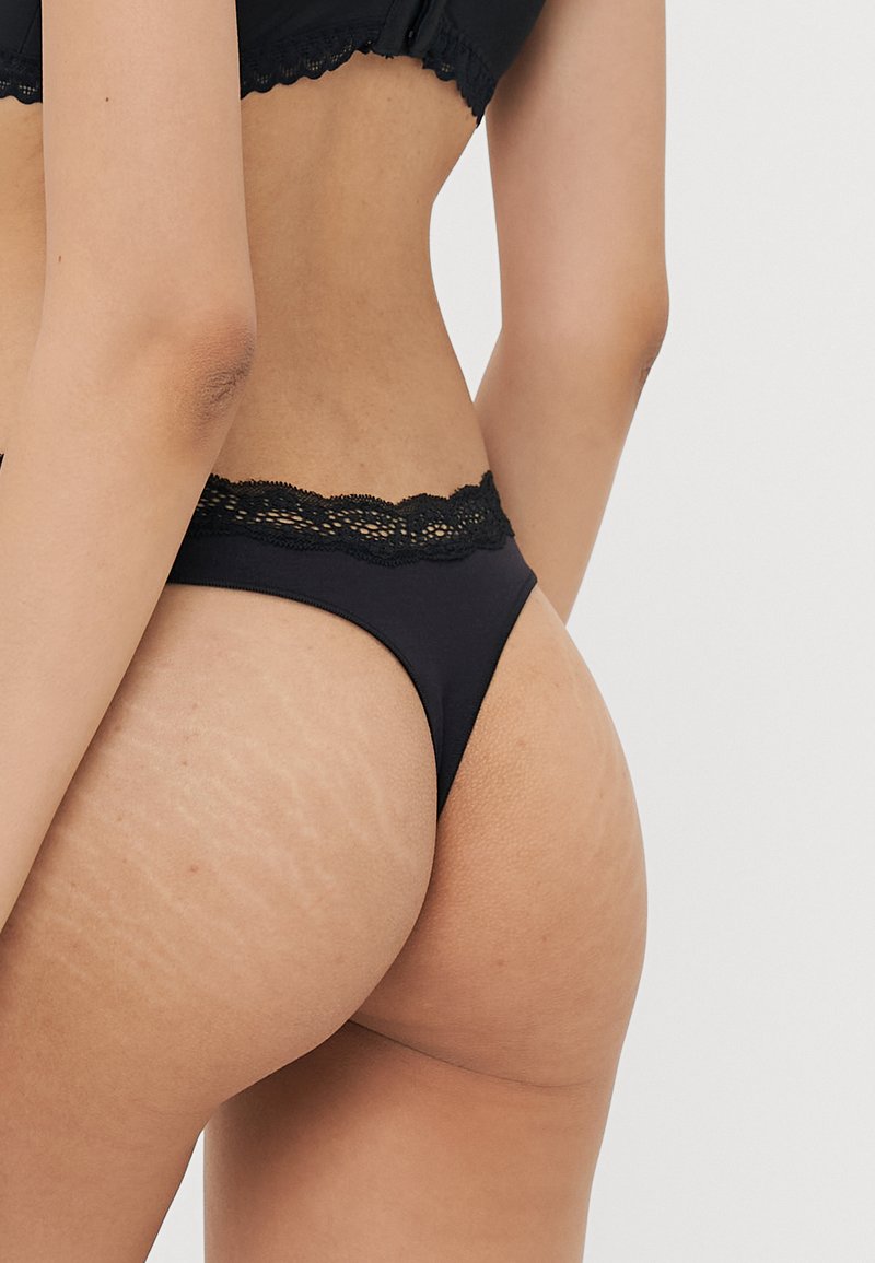 Tanga negra de encaje con un diseño minimalista y tela suave. Presenta un ajuste de cadera baja y detalles delicados en la cinturilla.